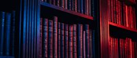 Shelves filled with antique books illuminated by neon blue and red lighting, creating a moody atmosphere suitable for library, bookstore, education, and literary design projects.