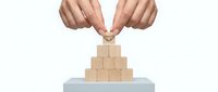 Two hands placing wooden block on pyramid structure, business growth and success concept for corporate strategy.
