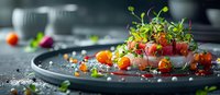 Fresh tuna tartare with microgreens, cherry tomatoes and citrus pearls on dark plate, fine dining presentation with modern molecular gastronomy elements.