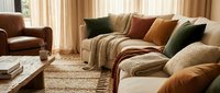Cozy modern living room interior with beige sectional sofa, colorful throw pillows, woven rug, and warm natural lighting for home decor inspiration.