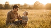 Father and young son bonding in golden wheat field during sunset, sharing tender moment together in rural countryside setting for family lifestyle content.