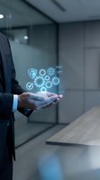 Businessman holding holographic digital icons with gears, shield, globe and checkmark in modern office environment representing technology solutions.