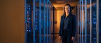 Professional Asian businesswoman standing confidently in modern data center server room with blue LED lighting for technology and corporate concepts.
