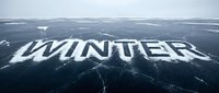 Word WINTER written in snow on cracked frozen lake surface under overcast sky, cold season concept for banners, cards, and seasonal designs.