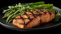 Grilled salmon fillet with fresh asparagus spears on dark plate, healthy protein meal with herbs and grill marks for restaurant menu and cooking content.
