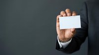 Businessman in dark suit holding blank white business card, closeup of hand presenting empty card for corporate branding and contact information.