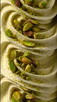 Creamy soft serve ice cream swirls topped with crushed pistachios and pistachio powder, macro food photography showing detailed texture and garnish.