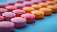 Colorful pharmaceutical pills arranged in diagonal rows on blue background, selective focus on pink and orange medicine tablets creating geometric pattern.