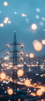 High voltage power line tower silhouette against evening city lights with dreamy bokeh effect creating magical atmosphere in blue and orange tones.