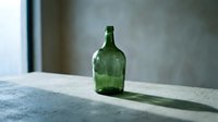 Vintage green glass bottle with shadow on concrete surface, suitable for still life, product photography, and design projects.