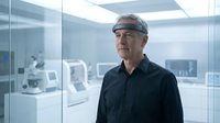 Middle-aged Caucasian male engineer or technician wearing safety headgear in modern laboratory or manufacturing facility with advanced equipment and glass partitions.