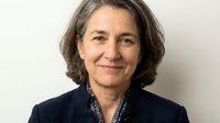 Professional mature woman with gray hair in business attire smiling confidently against neutral background for corporate and leadership concepts.