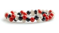 Elegant beaded bracelet featuring alternating red, black and white pearl-like spheres arranged in single strand against neutral background. Suitable for jewelry design.