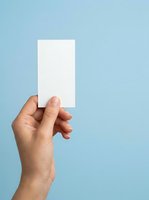 Hand holding blank white card against light blue background, suitable for business branding, marketing mockups, and promotional material presentations.