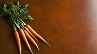 Fresh organic carrots with green tops on rustic brown background, raw vegetables arranged in minimalist composition for food photography and healthy eating concept.