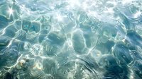Sunlight dancing on rippling turquoise water surface creates abstract patterns and reflections. Underwater view of gentle waves with natural light rays penetrating crystal clear sea.