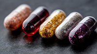Colorful transparent medicine capsules filled with glitter and sparkles arranged in row on dark background, macro photography for pharmaceutical design.
