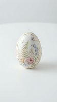 Elegant porcelain Easter egg with delicate floral pattern featuring roses, ferns and wildflowers on white background for spring holiday decorations.