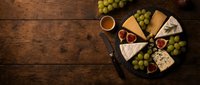 Assorted cheeses, fresh grapes, and figs arranged on wooden board with knife for wine tasting and entertaining.