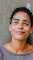Young woman with dark hair and olive skin tone smiling with eyes closed against textured concrete wall, expressing joy and contentment for lifestyle and wellness campaigns.