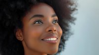 Young African American woman with natural afro hair smiling confidently against soft background, radiating joy and positivity for wellness, beauty, or lifestyle content.