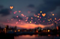Romantic heart-shaped bokeh lights floating over blurred city skyline at sunset. Love concept for Valentine's Day, wedding invitations, dating apps.