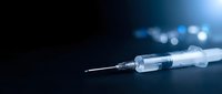Medical syringe with needle on dark blue background with bokeh lights for healthcare and vaccination concepts in clinical setting.