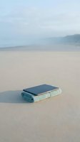 Smartphone and towel resting on sandy beach with calm ocean and misty coastline in background, representing vacation, travel, relaxation, and digital detox themes.