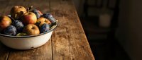 Fresh apples and plums in white bowl on rustic wooden table, ideal for food styling, recipe blogs, farmers market promotions, and culinary content.