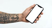 Tattooed male hand holding smartphone with blank white screen mockup for app presentation and mobile interface design projects.