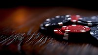 Casino poker chips stacked on dark wooden table with dramatic lighting and shallow depth of field creating atmospheric gambling environment.