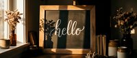 Rustic wooden framed chalkboard sign with hello lettering in warm sunlight, surrounded by dried flowers and vintage decor on a cozy shelf.