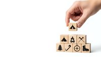 Hand placing wooden cube with camping tent icon completing adventure travel symbol pyramid on white background for outdoor recreation planning.