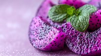 Fresh dragon fruit slices with vibrant pink flesh and black seeds garnished with mint leaves on pink background, macro food photography for healthy eating concept.