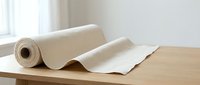 Roll of white paper unrolling on wooden table in bright room with natural light from window creating clean minimalist workspace for crafts and projects.