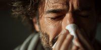 Middle-aged man with beard sneezing into tissue, showing cold or flu symptoms with dramatic lighting for health and wellness concepts.