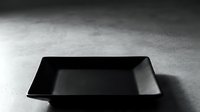 Black empty rectangular tray on concrete surface casting shadow, suitable for product mockups, food styling, and commercial advertising layouts.