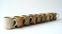 Row of handmade ceramic coffee mugs in earth tones with speckled glaze finish, artisan pottery collection for kitchen and dining decor.