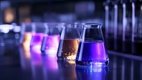Laboratory glassware with colorful liquid chemicals in flasks glowing with vibrant purple and pink hues against dark background, scientific research concept.