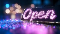 Glowing neon open sign with pink and blue bokeh lights creating magical atmosphere on dark background. Modern business concept for night establishments.