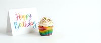 Rainbow cupcake with swirled cream topping and sprinkles beside a colorful Happy Birthday greeting card on white background.