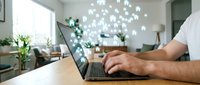 Professional man working on laptop computer with digital network icons floating above screen representing connectivity and technology in modern office workspace.