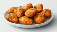 Crispy golden chicken nuggets garnished with fresh parsley on white ceramic plate, close up view of homemade breaded meat appetizers against light background.