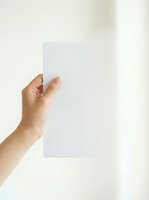 Close-up of a Caucasian hand holding a blank white card or paper against a neutral background, suitable for mockups, branding, and marketing materials.