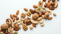 Mixed nuts and seeds collection scattered on white background featuring almonds walnuts pecans cashews pistachios hazelnuts for healthy snacking and cooking.