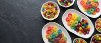 Colorful breakfast cereal rings in white bowls on dark slate background. Rainbow colored cereal loops arranged for morning meal advertising and food photography.