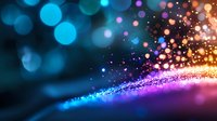 Magical glowing particles with blue and golden bokeh lights creating abstract wave pattern on dark background, festive sparkle effect for celebrations.
