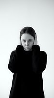 Young woman covering ears with hands in black sweater expressing stress anxiety or noise sensitivity on white background studio portrait.