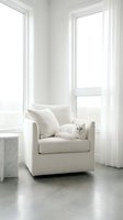 Fluffy white Persian cat resting on a cream armchair in a bright minimalist living room with large windows and sheer curtains.
