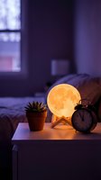 Glowing moon lamp on bedside table with succulent plant and alarm clock creating cozy bedroom atmosphere at night for relaxation and sleep.